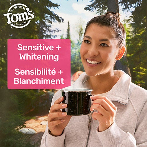 A woman smiling and holding a steaming mug outdoors in a wooded setting, illustrating sensitivity relief while enjoying hot beverages. A pink text box reads "Sensitive + Whitening" in English and French.